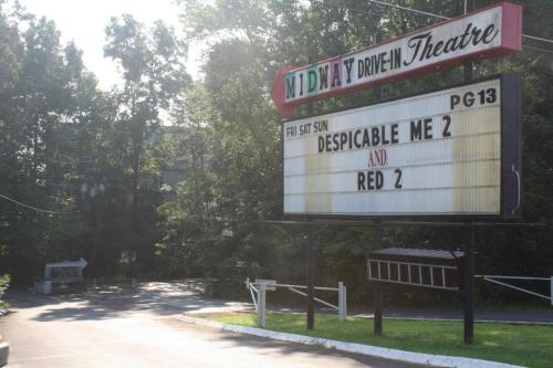 Sign for Midway Drive-In Theatre displaying "Despicable Me 2" and "Red 2" showings, surrounded by trees.