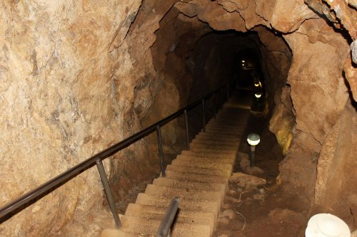 A dimly lit stone staircase descends into a rocky cave, with lights illuminating the path.