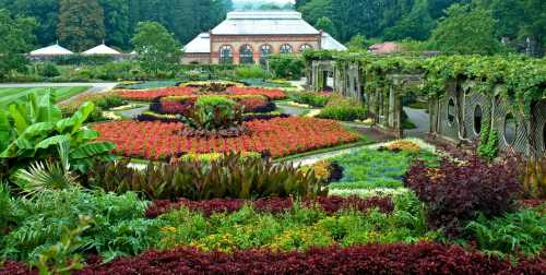 A vibrant garden with colorful flower beds and lush greenery, featuring a glass conservatory in the background.