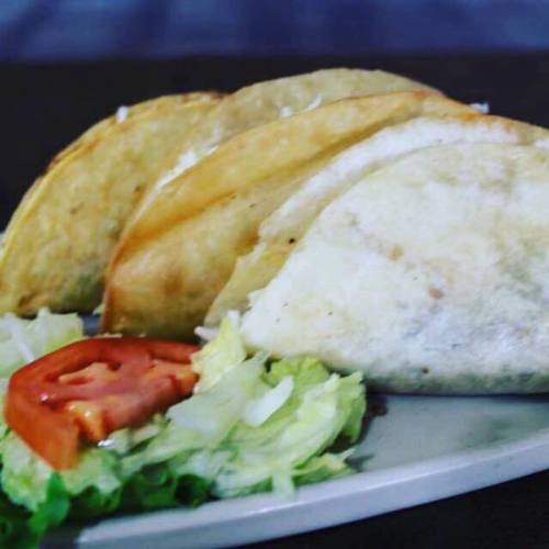 Three crispy tacos on a plate, accompanied by lettuce and tomato slices.