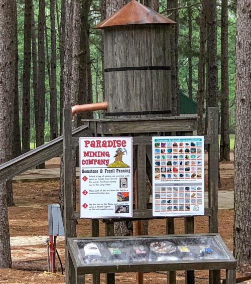 Sign for Paradise Mining Company with information on gemstone and fossil panning, surrounded by trees.