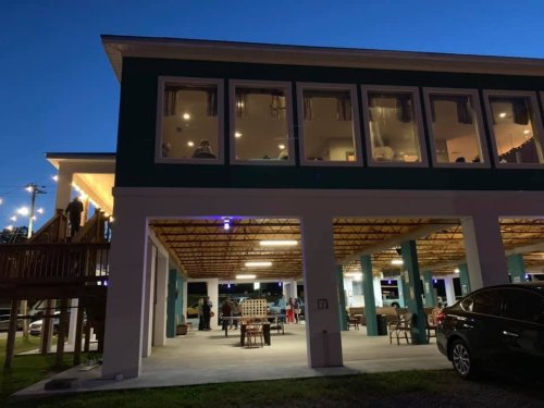 A two-story building at dusk, featuring large windows and outdoor seating under a covered area.