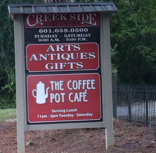 Sign for Creek Side Mercantile featuring "Arts, Antiques, Gifts" and "The Coffee Pot Café" with lunch hours listed.