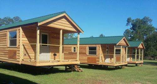 Three wooden cabins with green roofs, set on a grassy area under a clear blue sky.