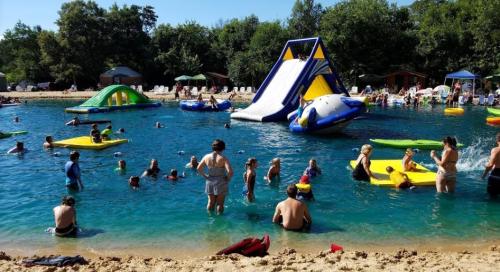 A busy water park scene with people swimming, playing on inflatables, and a large slide by the shore.