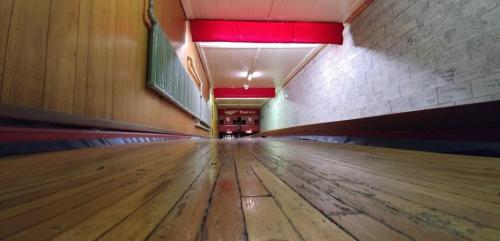 A long, wooden hallway with red accents and a textured wall, leading to a distant entrance.