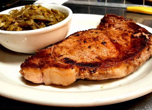 A grilled pork chop served with a side of green beans on a white plate.