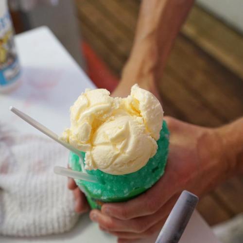 A person holds a cup of blue shaved ice topped with three scoops of vanilla ice cream.