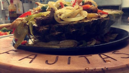 Sizzling fajitas served in a pineapple, topped with onions and bell peppers on a wooden platter.