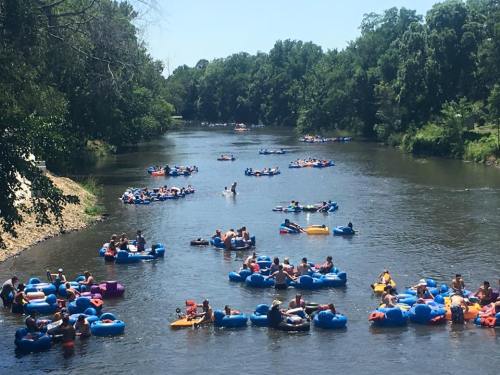 A busy river scene with many people floating on colorful inner tubes under a clear blue sky.