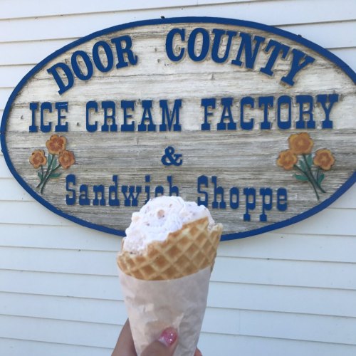 A hand holding a waffle cone filled with ice cream in front of a sign for Door County Ice Cream Factory & Sandwich Shoppe.