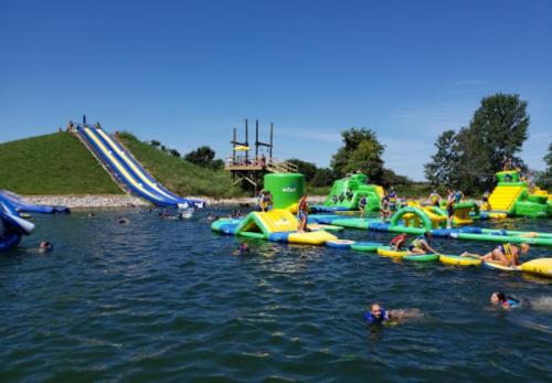 A vibrant water park scene with inflatable slides and structures, people swimming, and a clear blue sky.