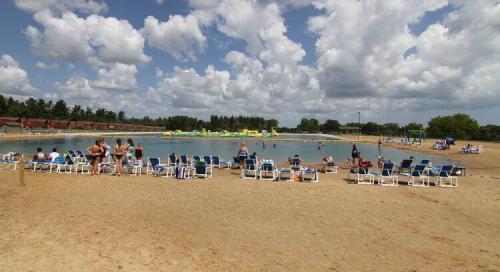 A sandy beach with lounge chairs, people swimming, and inflatable water attractions under a cloudy sky.