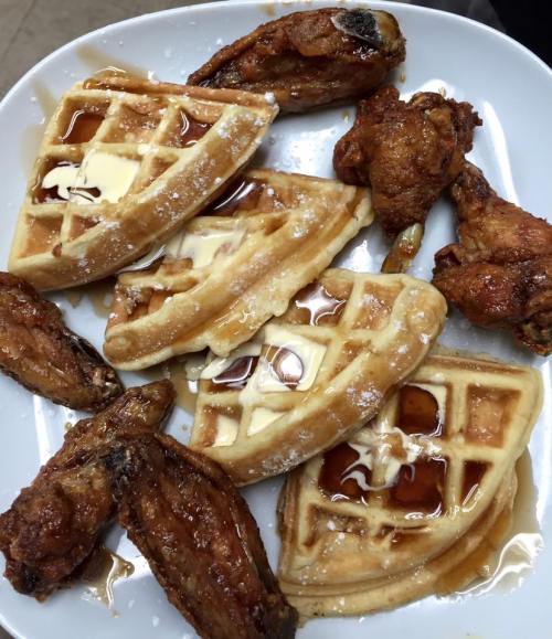 A plate of waffles topped with butter and syrup, accompanied by crispy chicken wings.