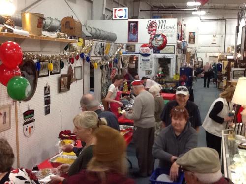 A bustling indoor market with people enjoying food, festive decorations, and holiday-themed displays.