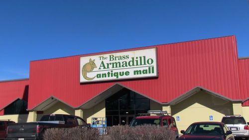 Exterior of The Brass Armadillo Antique Mall, featuring a red roof and sign, with parked cars in front.