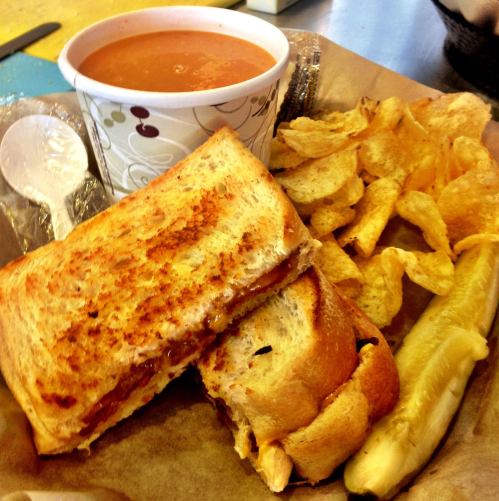 A plate featuring a grilled cheese sandwich, a cup of tomato soup, potato chips, and a pickle.