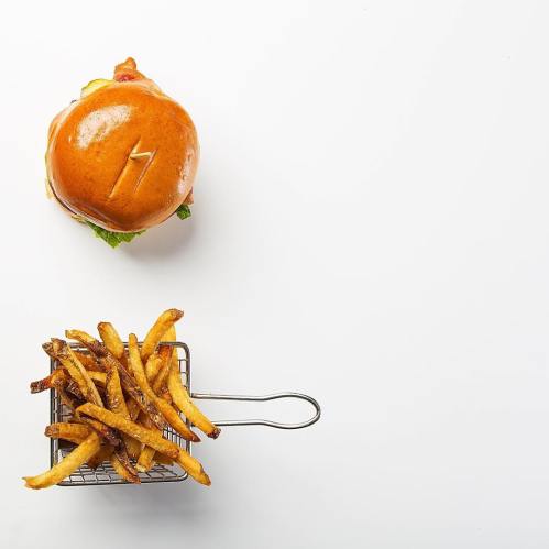A burger with a number 7 on top, next to a basket of crispy French fries on a white background.