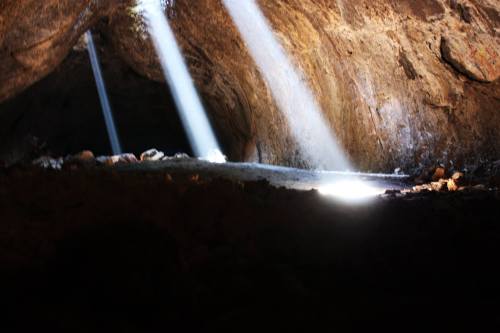 Light beams streaming through a cave entrance, illuminating the rocky interior and creating a mystical atmosphere.