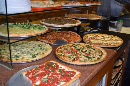 A display of various pizzas on a counter, featuring different toppings like vegetables, meats, and sauces.