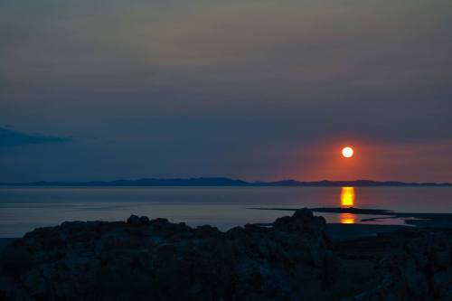 A serene sunset over a calm lake, with mountains in the distance and a glowing reflection on the water.