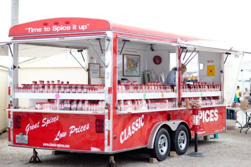 A red spice trailer with jars of spices displayed, featuring a sign that says "Time to Spice it up!" and a vendor inside.