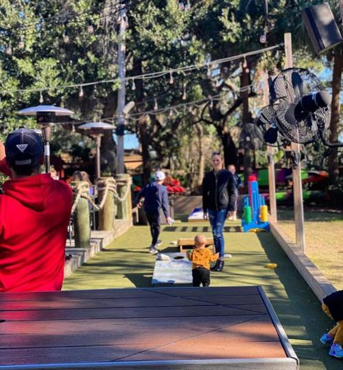 A playground scene with children playing, surrounded by trees and outdoor seating. Bright and sunny day.