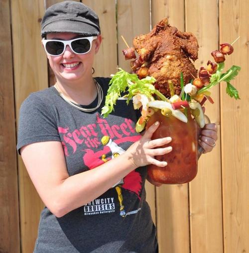 A person in sunglasses holds a large, extravagant drink topped with fried chicken and various garnishes.