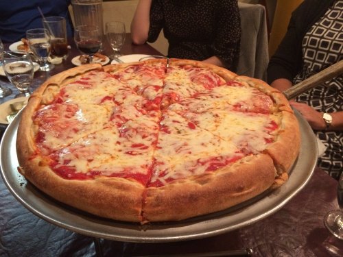 A large, cheesy pizza with a golden crust, sliced into eight pieces, served on a round metal tray.