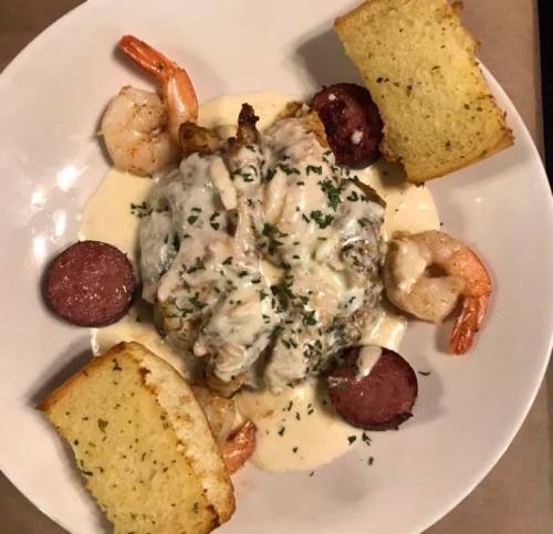 A plate of seafood featuring shrimp, sausage, and creamy sauce, served with slices of garlic bread.