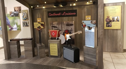 Display of musical instruments from Southwest Louisiana, including guitars, drums, and a washboard, in a rustic setting.