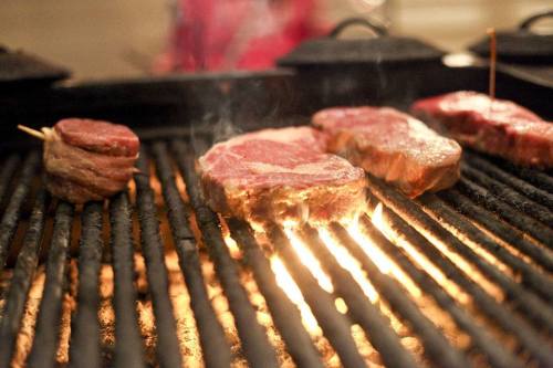 Grilling steaks on a barbecue, with smoke rising and flames visible between the grill grates.