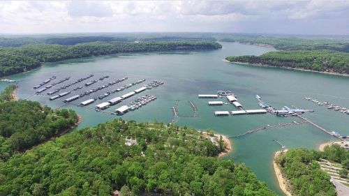 Aerial view of a marina surrounded by lush green hills and calm blue waters under a cloudy sky.