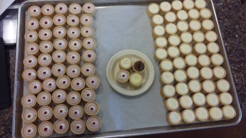 A tray of small dessert cups arranged in rows, with a few on a plate in the center, featuring red and white toppings.