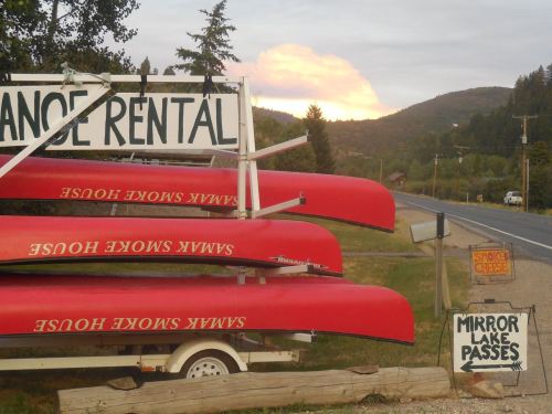 A row of red canoes stacked on a trailer, with a scenic mountain backdrop and a sunset in the distance.