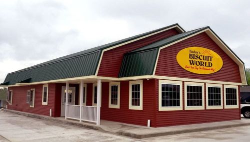 A red and green building with a sign reading "Tudor's Biscuit World," featuring large windows and a welcoming entrance.