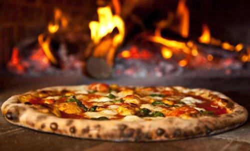 A freshly baked pizza with melted cheese and toppings, placed in front of a glowing wood-fired oven.