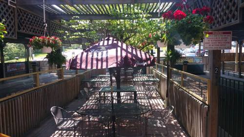 Outdoor dining area with tables, chairs, and a large umbrella, surrounded by hanging plants and greenery.