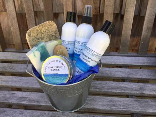 A metal bucket filled with bath products, including shampoo bottles, soap bars, and a candle, on a wooden surface.