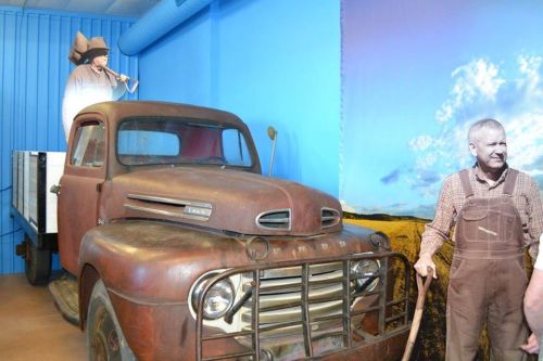 A vintage truck displayed in a museum, with two life-sized figures of farmers in a blue room.