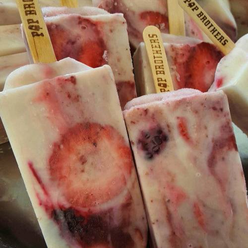 Colorful fruit popsicles with wooden sticks, featuring strawberries and other berries, arranged closely together.