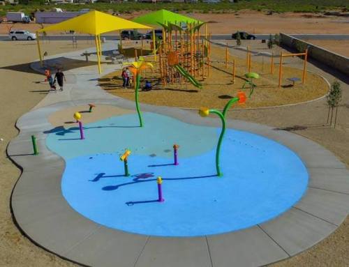 A colorful playground with water features, slides, and shaded areas, set in a sandy outdoor space.