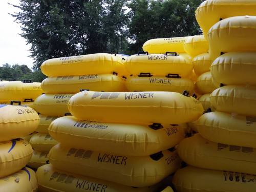 A stack of bright yellow inflatable rafts labeled "WISNER" arranged neatly outdoors among trees.