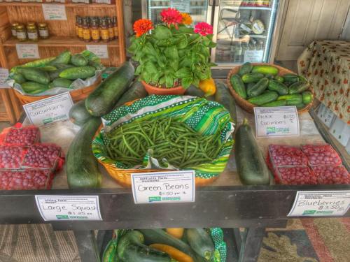 A farm stand display featuring cucumbers, green beans, squash, raspberries, and blueberries with price tags.