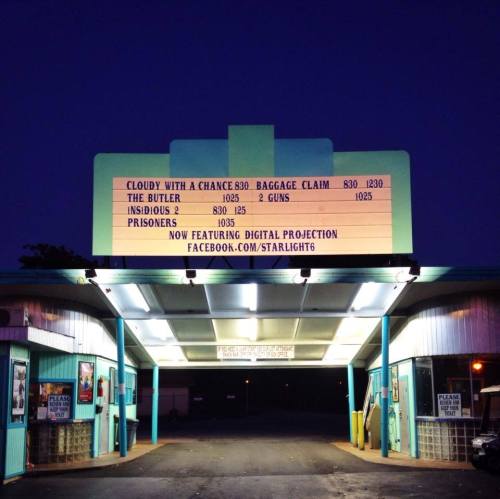 A vintage movie theater marquee displays showtimes for various films against a twilight sky.