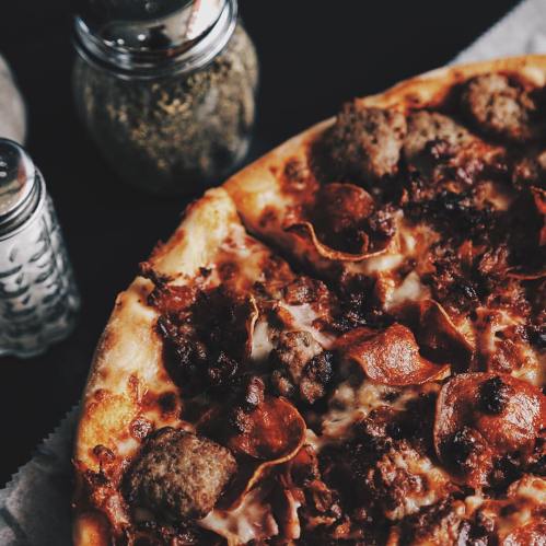 A close-up of a meat-lover's pizza topped with pepperoni, sausage, and melted cheese, with seasonings in the background.