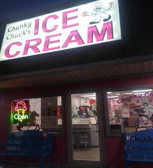 Sign for "Chunky Chuck's Ice Cream" shop, brightly lit with an open sign, featuring a playful ice cream character.