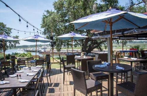 Outdoor dining area with tables, umbrellas, and a view of the water, surrounded by trees and string lights.