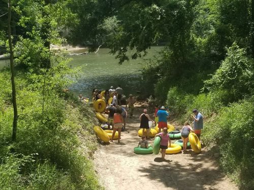 A group of people preparing to go tubing on a river, surrounded by trees and greenery.