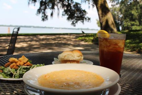 A bowl of soup, salad, rolls, and iced tea on a table by a lake, with trees in the background.